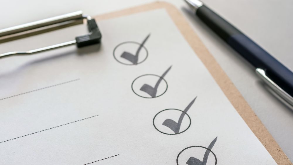 Checkliste mit abgehakten Punkten auf einem Klemmbrett und Kugelschreiber, symbolisiert Organisation und Planung.