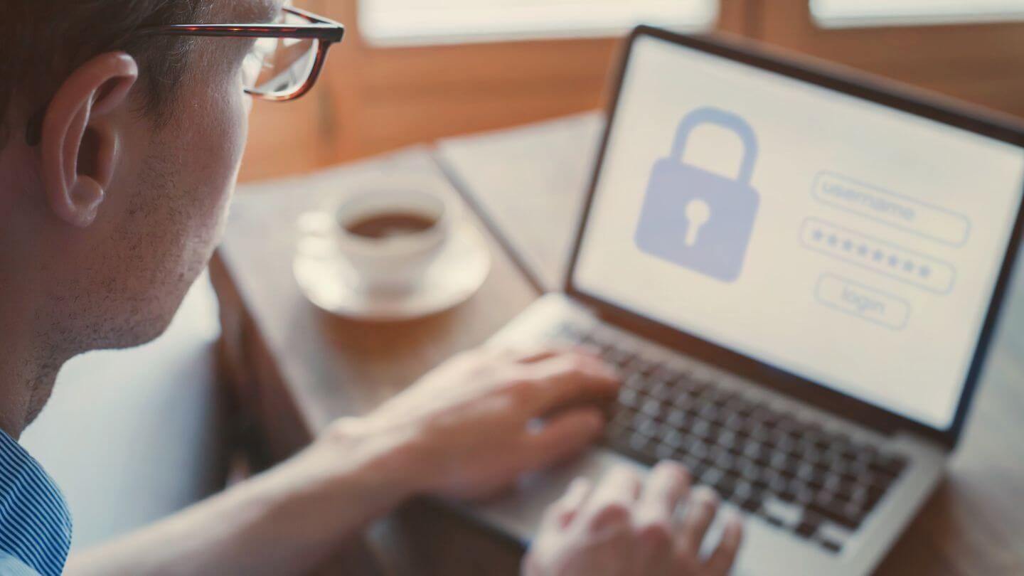 Mann mit Brille sitzt an einem Laptop mit einem Anmeldebildschirm, der ein Schloss-Symbol und Passwortfelder zeigt.