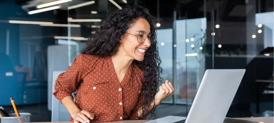 Glückliche Frau im modernen Büro freut sich vor Laptop über Erfolg oder Schulung.