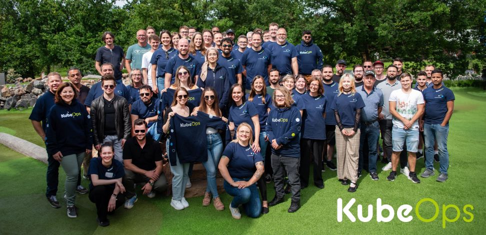 Gruppenfoto des KubeOps-Teams mit Teammitgliedern in KubeOps-T-Shirts vor einer grünen Outdoor-Kulisse.
