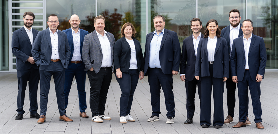 Gruppenfoto des KubeOps-Management-Teams vor einer verglasten Fassade.